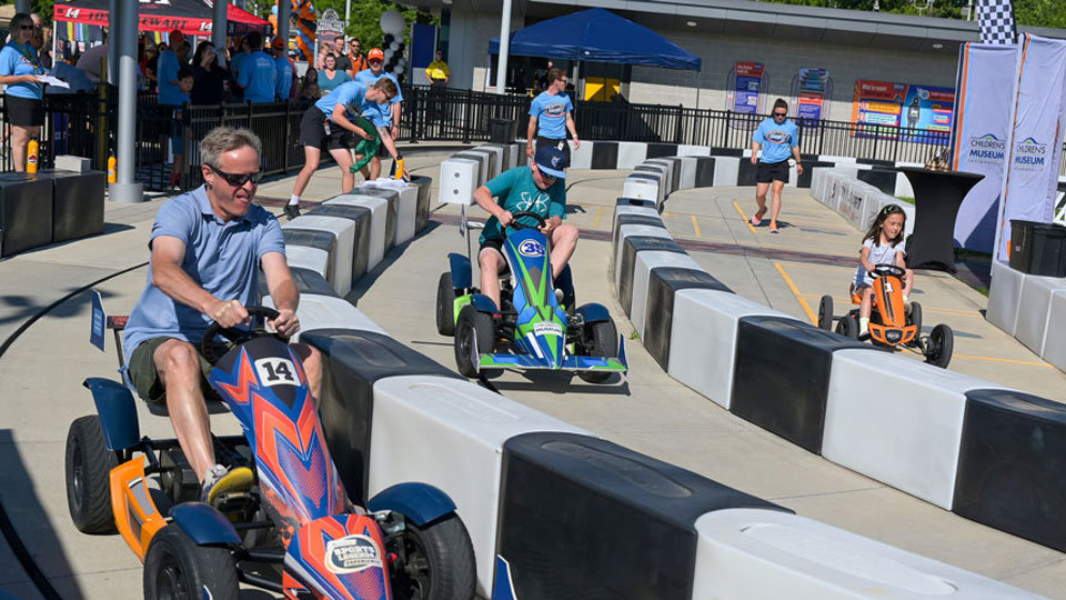 An adult races against multiple kids on a small pedal car race track